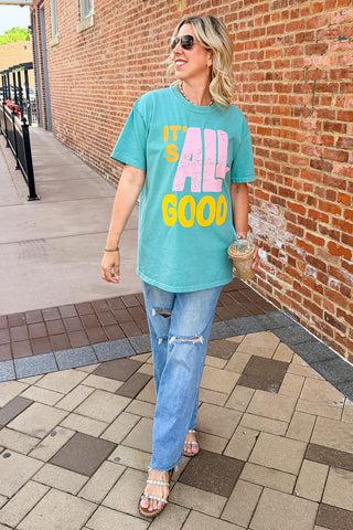 Woman wearing a colorful t-shirt with text standing on a sidewalk next to a brick wall.